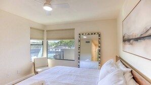 Ein Hotelzimmer mit Bett, Deckenventilator, Fenster mit Jalousien, Spiegel und einem Bild an der Wand.