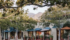 An outdoor seating area with umbrellas and potted plants, overlooking a mountainous landscape.