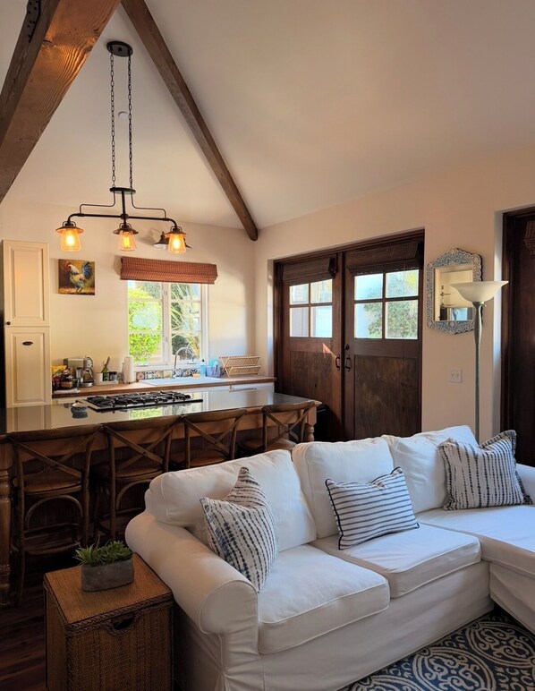 A cozy living room with a white sofa, wooden chairs, a kitchen area with a stove, and a dining table.