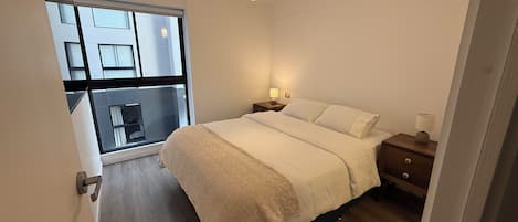 A bedroom with a bed, bedside tables, a lamp, and a view through a window.