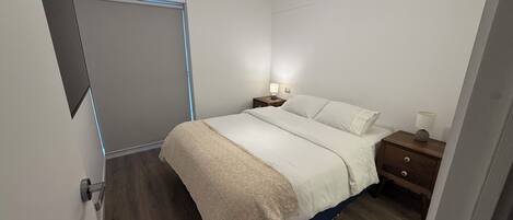 A bedroom with a bed, bedside tables, a nightstand, a lamp, and a door with a handle.