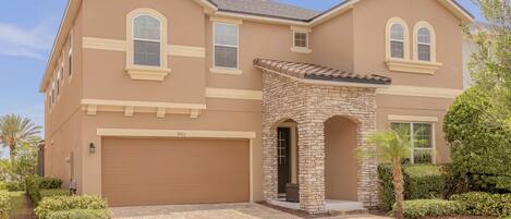 A two-story house with a stone archway entrance, a garage, and a well-maintained lawn.