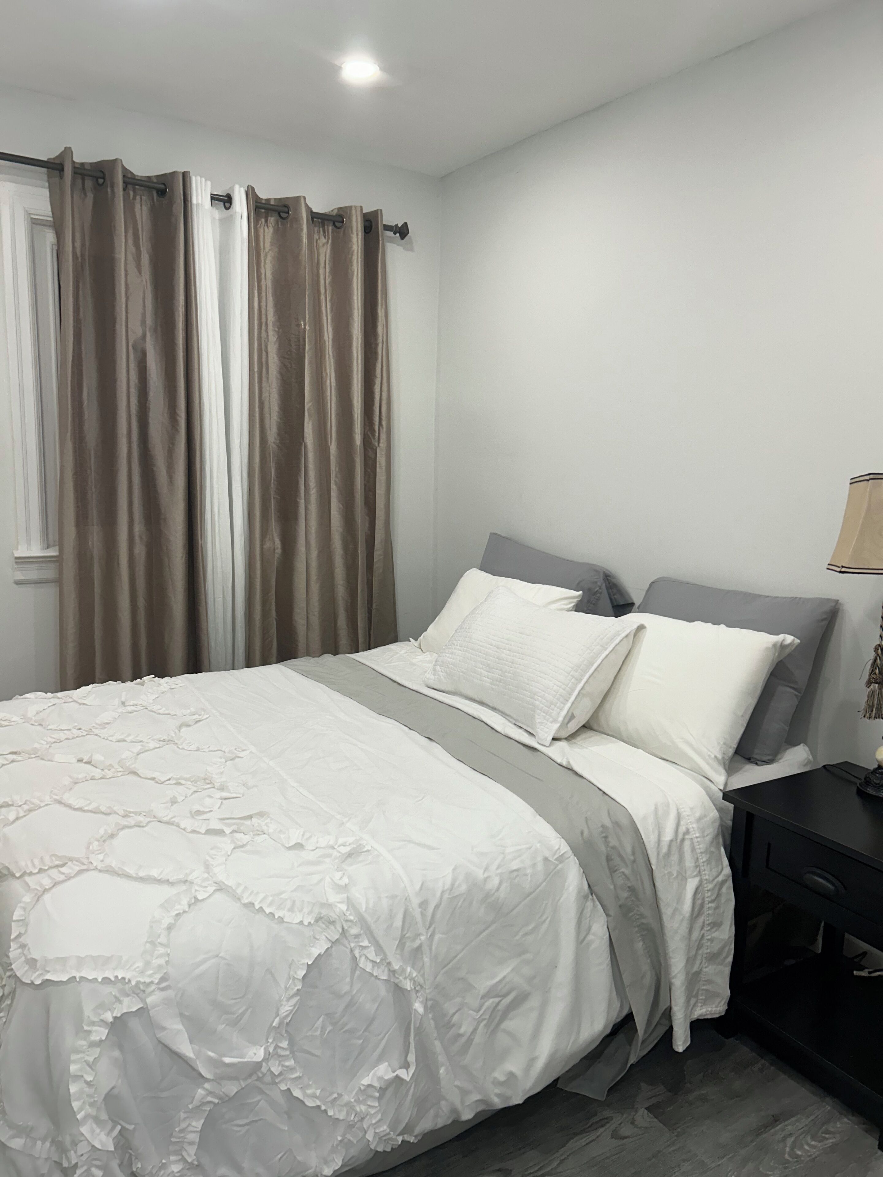 A bedroom with a bed, curtains, a nightstand, and a lamp.