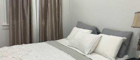 A bedroom with a bed, curtains, a nightstand, and a lamp.