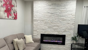 Un salon moderne avec un mur à l’aspect pierre, un téléviseur à écran plat fixé au mur, un canapé d’angle beige et un plaid à rayures.