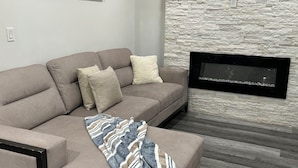 Un salon moderne avec un canapé d’angle beige, une cheminée et un mur à l’aspect pierre.