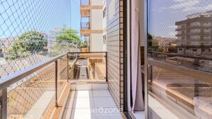 Ein Balkon mit Glasgeländer, Fliesenboden und Blick auf ein gegenüberliegendes Gebäude.