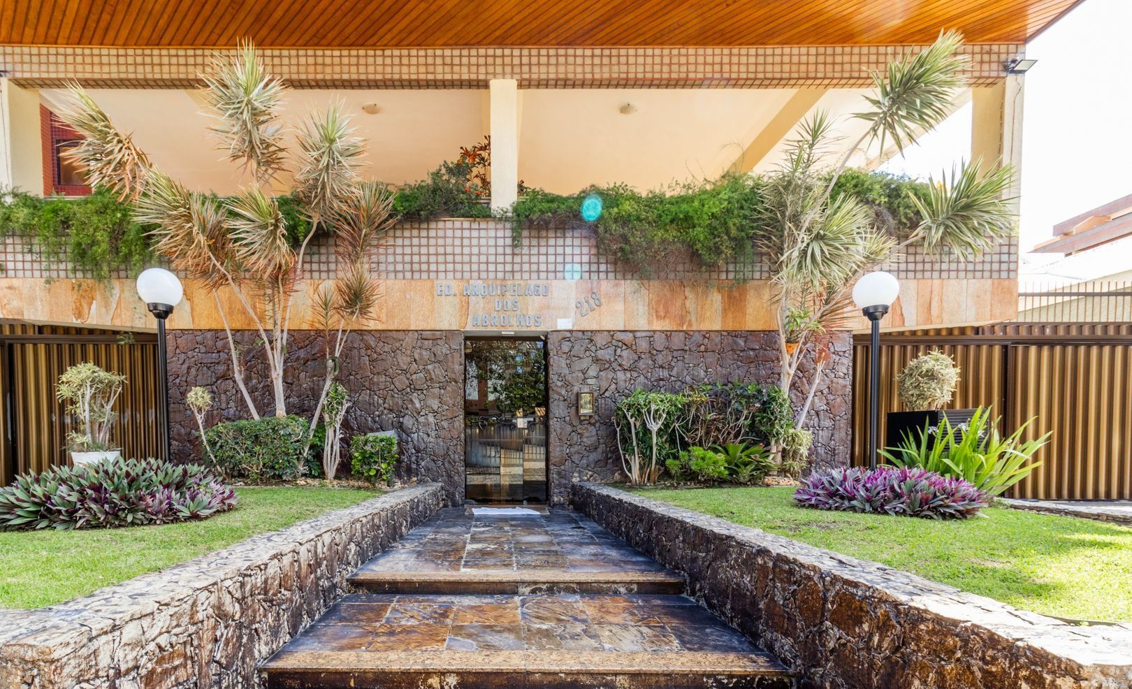 Una escalera de piedra que conduce a la entrada de un edificio, rodeada de plantas tropicales y un tejado de azulejos.