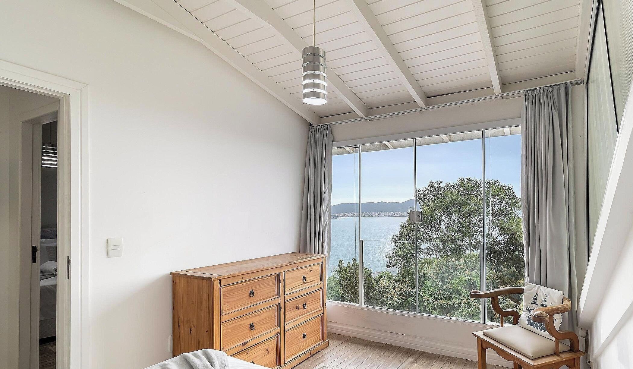 Una habitación con un ventanal grande, un aparador de madera, una silla y un ventilador de techo.