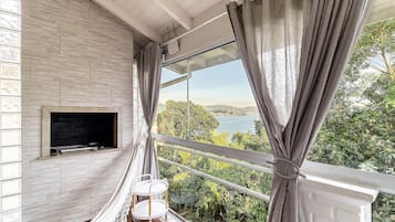 Un balcón con televisor, una hamaca y vistas a un lago.