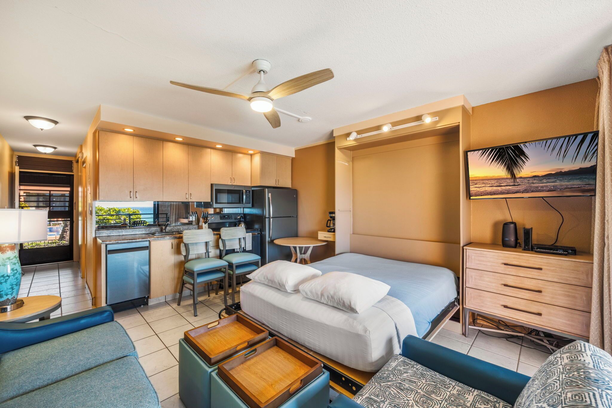 A compact hotel room with a kitchenette, a bed with a view, a desk, and a TV.