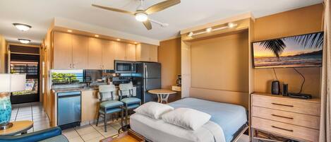 A compact hotel room with a kitchenette, a bed with a view, a desk, and a TV.
