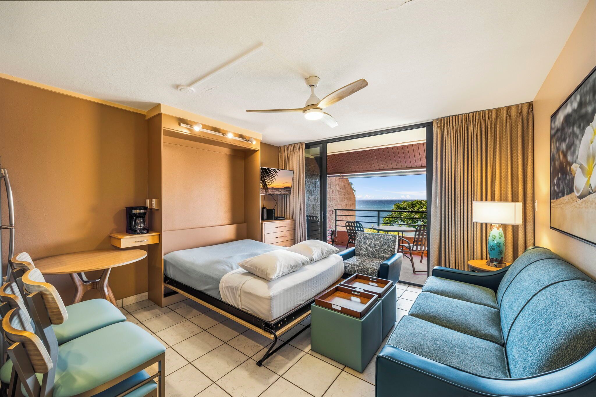 Habitación de hotel con cama, escritorio, sofá, ventilador de techo y vistas al exterior.