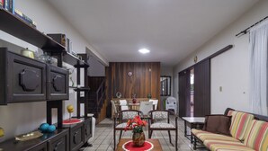 Una sala de estar con un sofá, una mesa de comedor con sillas, una escalera y una estantería.