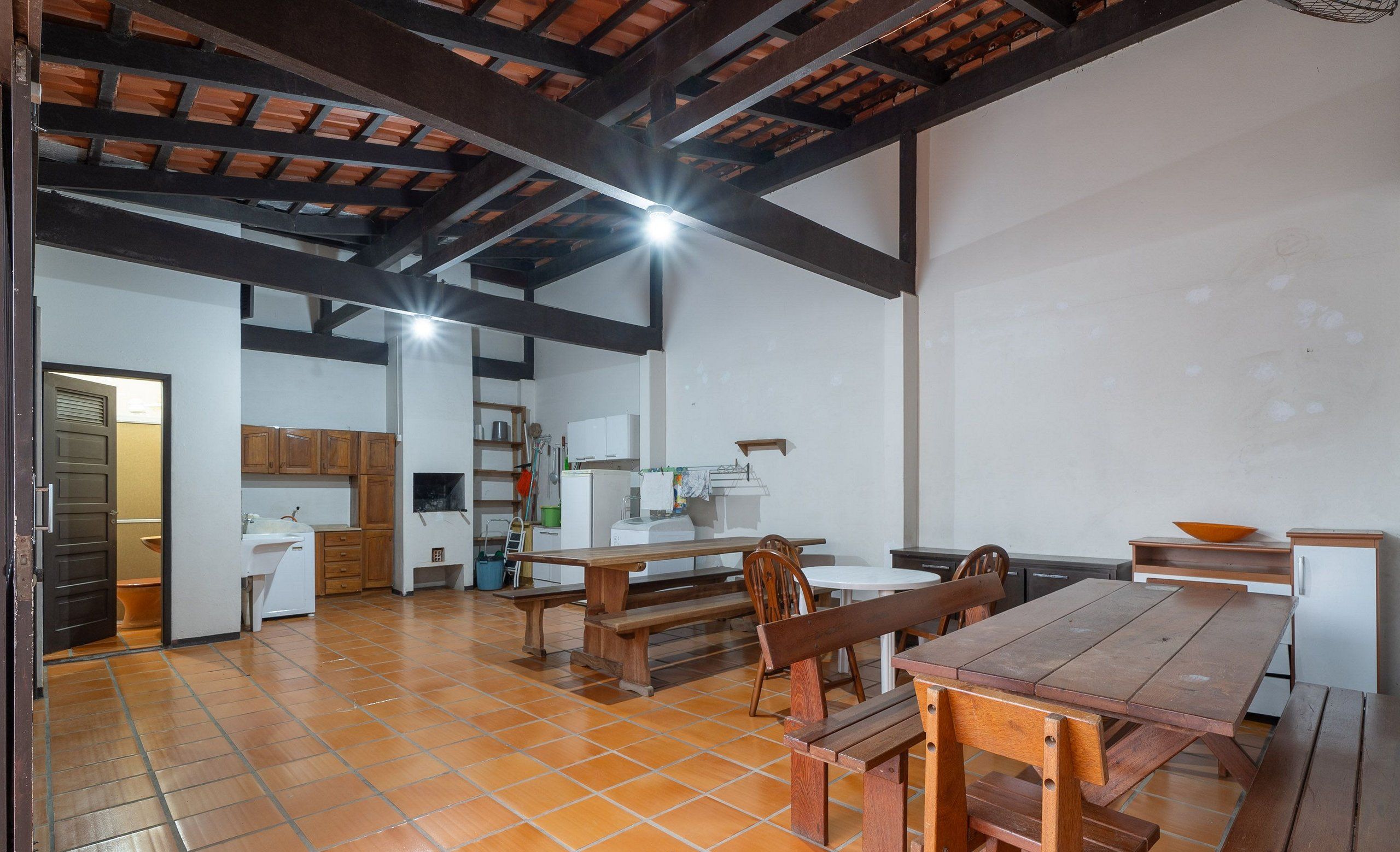 A spacious kitchen with wooden benches and a dining table, a white sink, and a tiled floor.