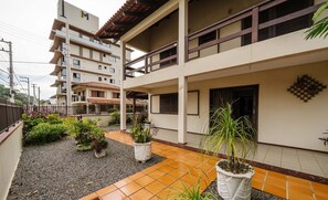 Um edifício residencial com vários andares, um pátio com azulejos, plantas em vasos e uma entrada visível.