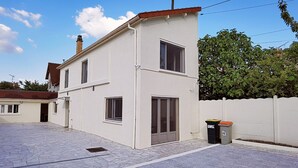 Una casa a due piani con patio in tegole, esterno bianco e tetto rosso.