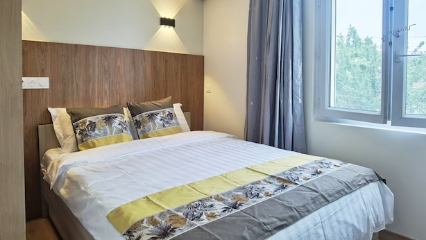 Una camera da letto con testiera in legno, un letto con lenzuola a motivi floreali, una finestra con tende e un condizionatore d'aria a parete.
