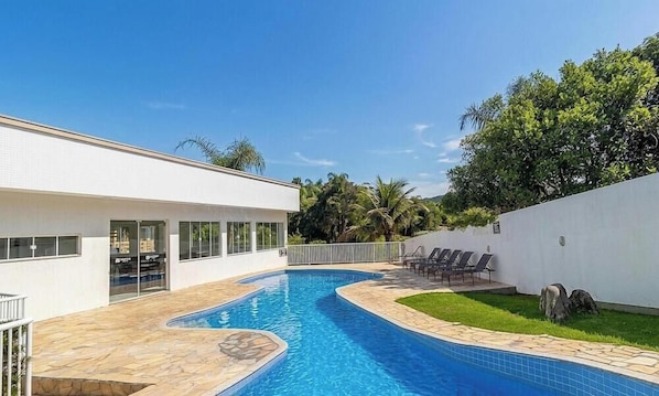 Une maison moderne dotée d’une piscine, d’un patio couvert et offrant une vue sur la verdure environnante.