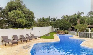 A swimming pool with lounge chairs, a stone wall, and tropical vegetation.