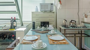 A modern kitchen with a glass dining table set for four, a microwave, a gas stove, and a coffee maker. - Aconchegante Loft Centro Hist Petrópolis ATO3091 (Petrópolis)