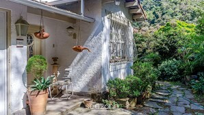 A house with a stone pathway leading to a door, surrounded by lush greenery and a mountain in the background. - Aconchegante Loft Centro Hist Petrópolis ATO3091 (Petrópolis)