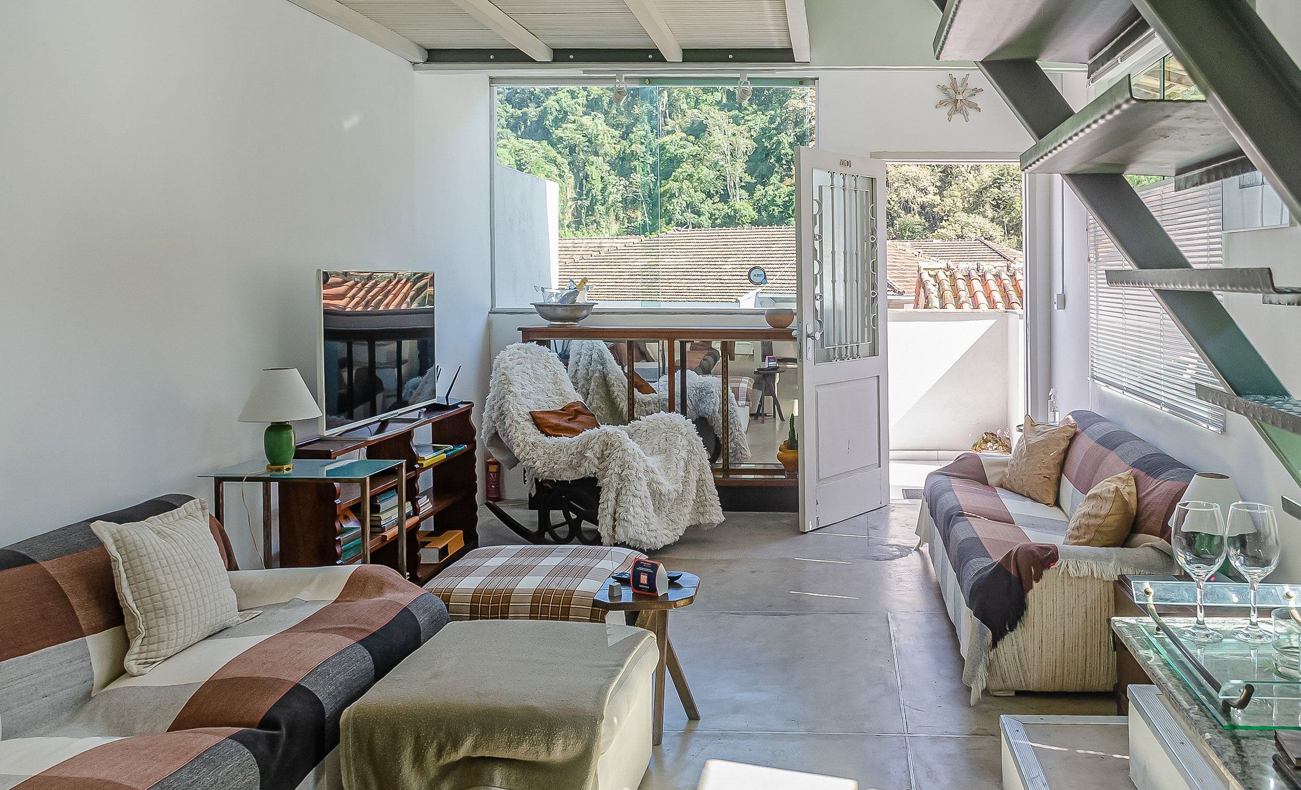 A cozy living room with a sofa, a chair, and a dining table. There is a bookshelf and a TV in the room.