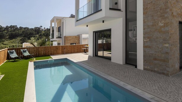 Ett modernt hus i två våningar med en swimmingpool, en balkong och en fasad av sten.