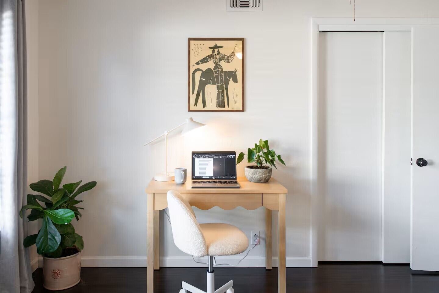 A desk with a laptop, a lamp, and a potted plant in a hallway.