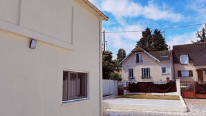 A residential area with a paved courtyard, a house with a tiled roof, and a clear sky. - New studio with AC / free charging parking（NO.5） (Villemomble)