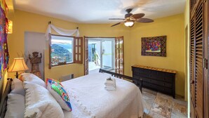 A bedroom with a bed, a nightstand, a dresser, a ceiling fan, and a window with a view of the outdoors. - Charming 2-bedroom, 2 bath condo in Mismaloya with AC, remodeled kitchen & baths (Mismaloya)