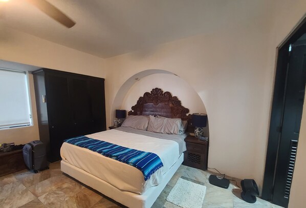 A bedroom with a bed, a nightstand, a suitcase, and a door.