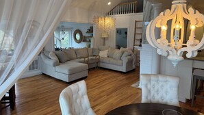 A spacious living room with a sectional sofa, a dining table, and a chandelier. - Designer 5 Bedroom, 3.5 bath home. Pool, Hot Tub, Pizza Oven, BBQ, bicycles. (Ocean Beach)
