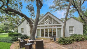 A house with a large glass door, a brick patio, and outdoor furniture. - Charming Sea Island Cottage • Steps to Beach • Sleeps 10 (Sea Island)
