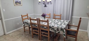Un coin repas avec une table recouverte d’une nappe à motifs floraux, entourée de chaises en bois.