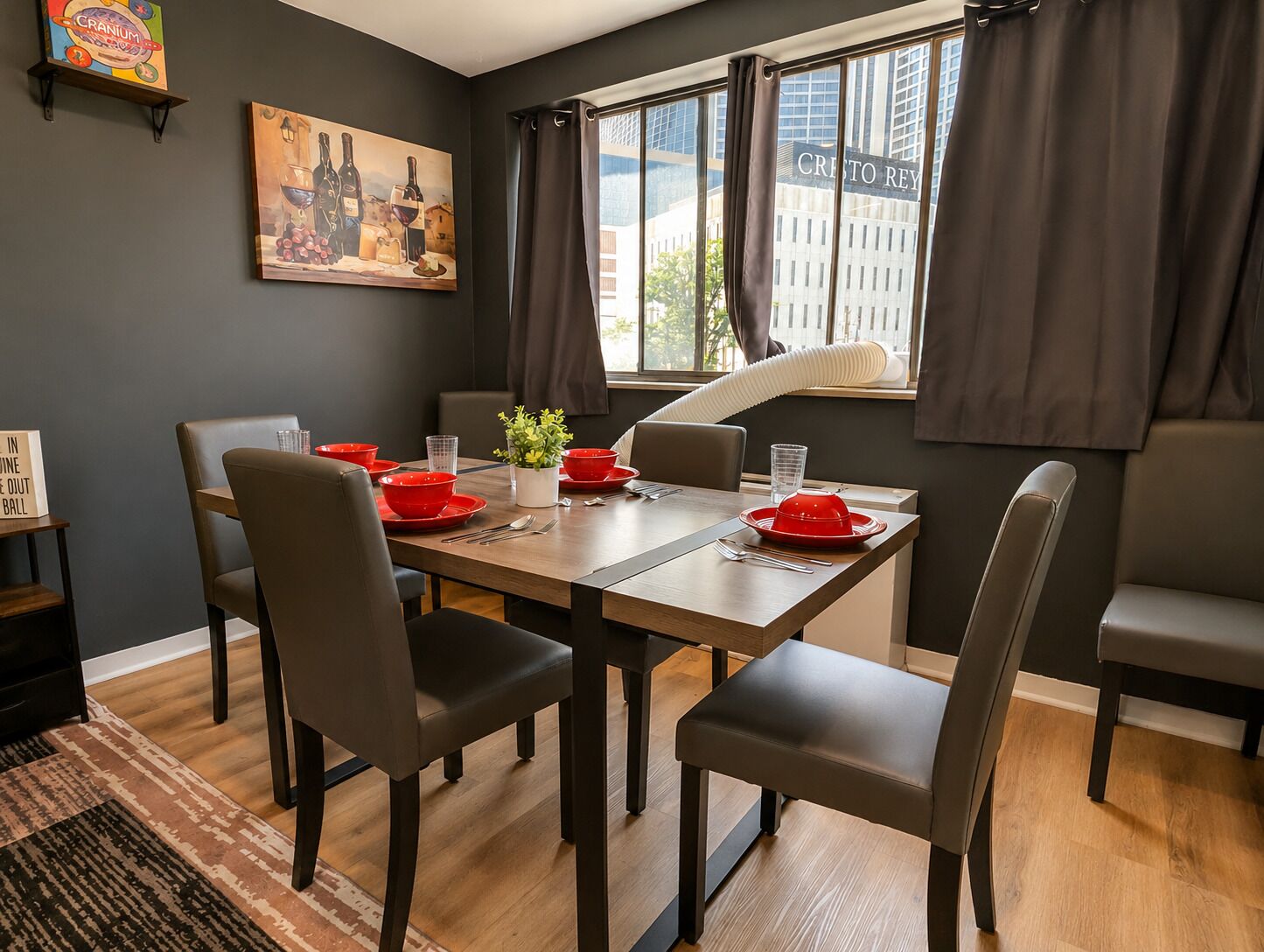 Un coin repas avec une table en bois, six chaises, de la vaisselle rouge, une plante en pot et un tableau accroché au mur.