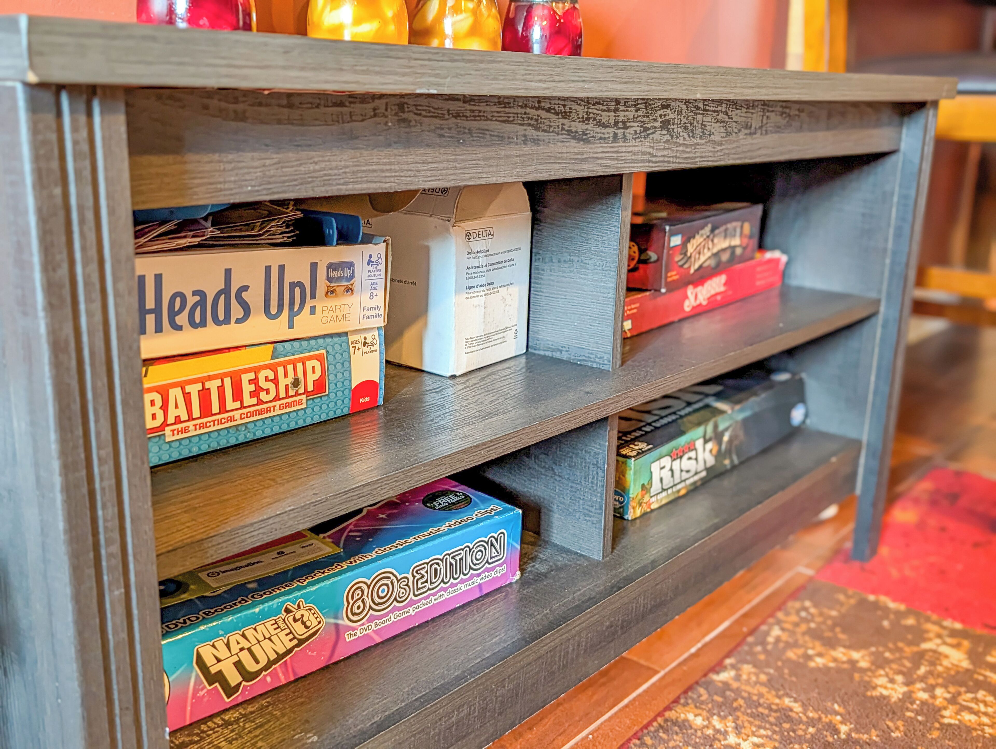 A wooden shelf with various board games, including 'Battleship,' 'Heads Up!,' and 'Risk.'