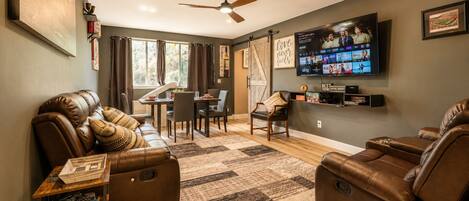 A living room with leather sofas, a TV, a dining area, and a ceiling fan.