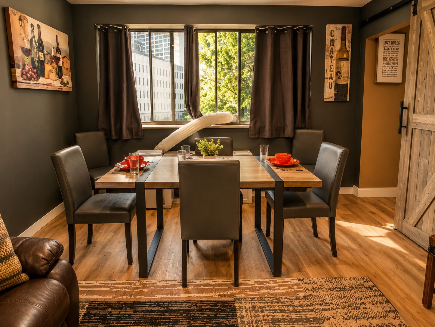A dining area with a wooden table, black chairs, a rug, and a view of buildings through large windows.