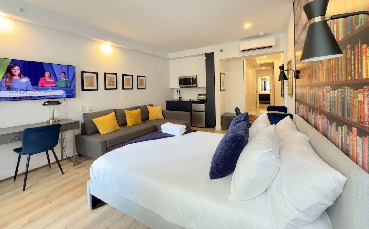 A modern hotel room with a large bed, a sofa, a desk, and a television.
