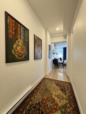 A hallway with framed artwork on the walls, a patterned rug on the floor, and a dining area in the distance. - Elegant Loft in Downtown Québec City (Québec City)