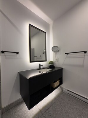 A modern bathroom with a black vanity, a large mirror, a round mirror, and towel racks.