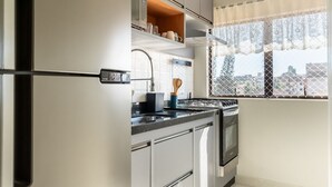 A modern kitchen with stainless steel appliances, a window with a view of buildings, and a decorative curtain. - Cozy Apartment Near the Beach Ubatuba Enu011 (Ubatuba)