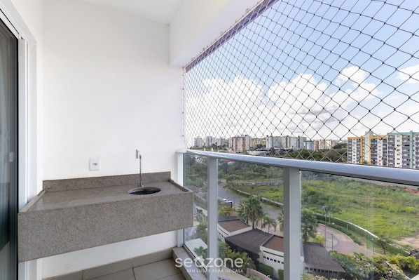 A balcony with a metal safety net, a small sink, and a view of a cityscape with buildings and greenery. - 3 Quartos no Evian Thermas Residence - Etha604 (Caldas Novas)