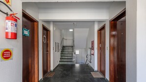 Un pasillo con suelo de baldosas oscuras, puertas de madera y un extintor de incendios en la pared.