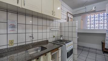 Una cocina con armarios blancos, estufa a gas, pileta y ventana con diseño de celosía.