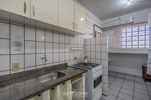 Een keuken met witte kastjes, een gasfornuis, een spoelbak en een raam met decoratieve roedeindes.