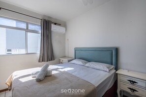 Une chambre d’hôtel comprenant un lit, une table de chevet, une commode, un appareil de climatisation et une fenêtre avec des rideaux.