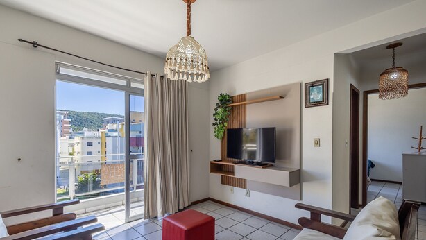 Un salón moderno con televisor, reposapiés rojo y balcón con vistas a edificios.