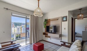 Un salon moderne avec un téléviseur, un pouf rouge et un balcon offrant une vue sur les immebles.